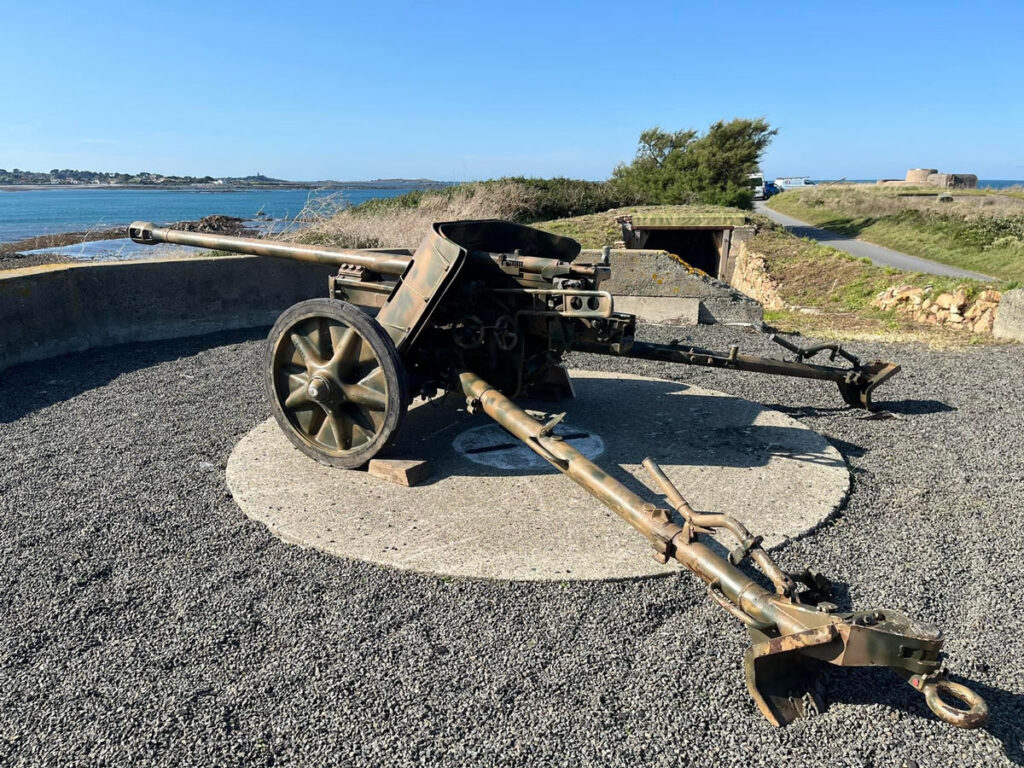 A large mounted WWII gun on a stone circle with a bunker in the background.